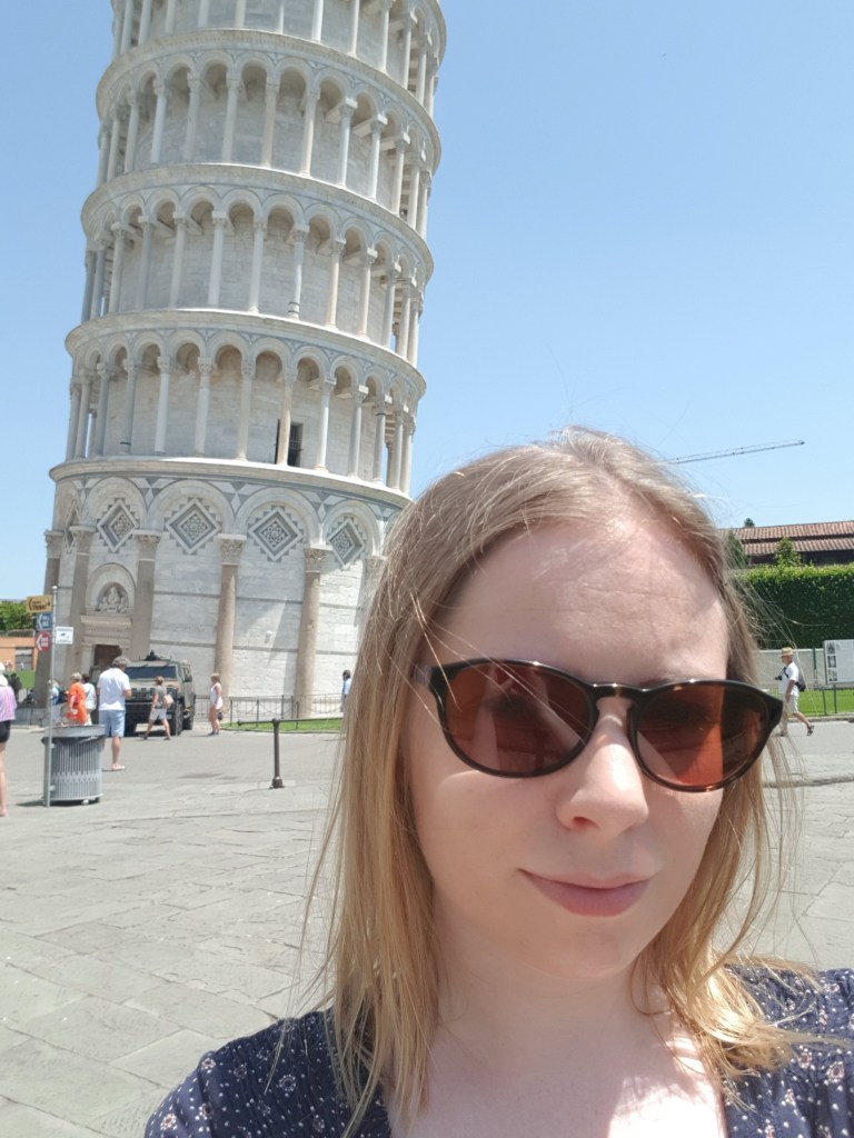 A girl stands in front of the Leaning Tower of Pisa