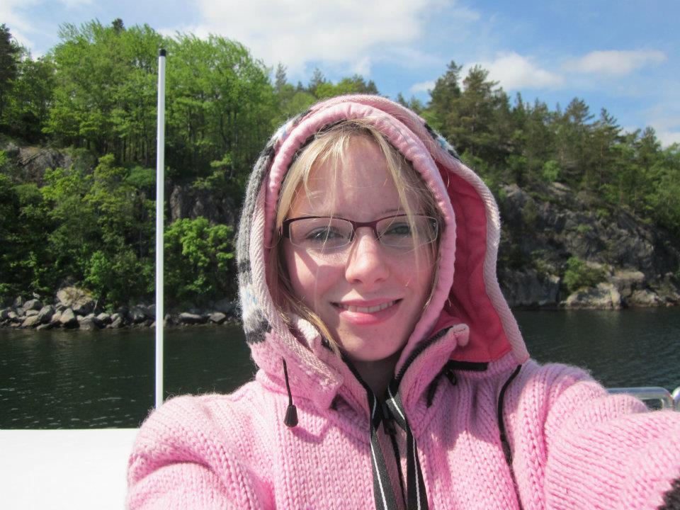 Girl wearing a thick pink jumper in the foreground with a rocky, tree lined landscape in the background